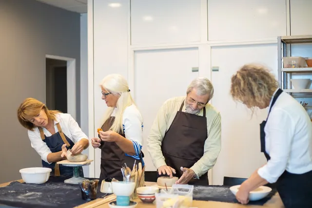 Four people shaping clay together in a pottery workshop